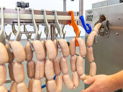 Prozesssicheres Aufhängen abgebundener Wurstprodukte auf die Haken der Aufhängeeinheit